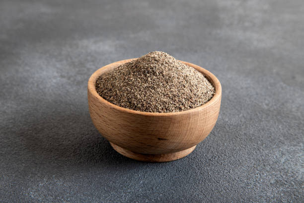 Bowl full of black peppercorns on black background